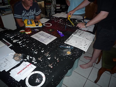 A gamer leaning over a table covered with a starfield battlemat, measuring and setting up movement markers for a fleet of starship miniatures